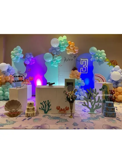A full view of the under-the-sea setup, featuring blue and orange balloons, coral and seashell props, and a neon number '3'.