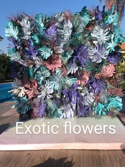 A modern art installation for a poolside party. This photo wall is made from monstera leaves painted in cool shades of blue, purple, and pink, creating a trendy and unique backdrop.