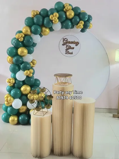 A stylish 'Growing Glow Bash' decoration with a sage green and gold balloon arch on a white circular backdrop.