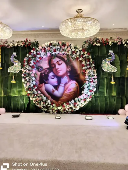 We also handle decorations for other family celebrations like baby showers. This Krishna-themed backdrop features a large floral ring around a central image, set against a traditional banana leaf wall.