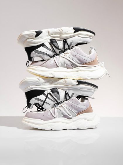 A minimalist shot of chunky white sneakers stacked on top of each other, creating a sculptural and abstract form.