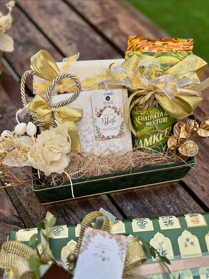 This wedding hamper, designed for Believe Weddings, showcases a modern Indian aesthetic with a green velvet tray and gold accents. It combines traditional snacks with elegant packaging and floral details for a sophisticated look.