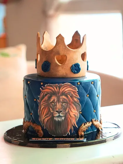 A regal and powerful lion-themed cake in deep blue with a quilted pattern, topped with a golden crown for a majestic celebration.