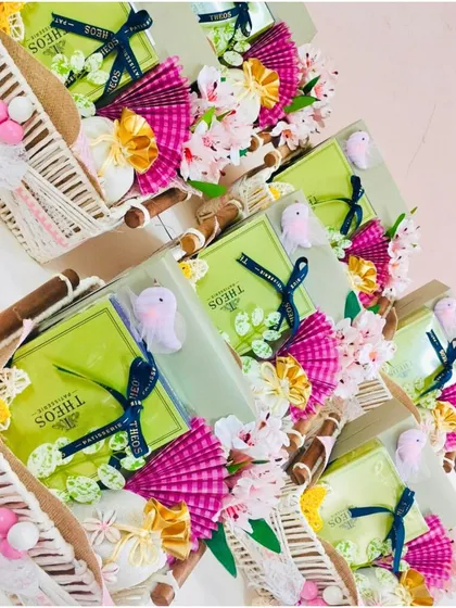 A collection of vibrant and festive baby shower return favors. These woven baskets are filled with goodies and decorated with bright pink and green floral details, creating a cheerful and celebratory gift for guests.
