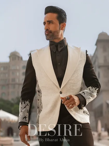 A modern twist on the classic tuxedo. This sleeveless white blazer is designed with sharp lapels and detailed embroidery on the sleeves of the underlying shirt, creating a layered, powerful look.