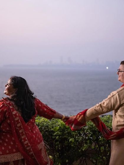 A romantic shot of a multicultural couple holding hands, overlooking the Mumbai sea and skyline at dusk.