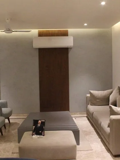 This view of the Hyderabad living room showcases the clean lines and balanced layout. A textured gray wall is complemented by a dark wood panel, creating a subtle feature behind the seating area. Cove lighting provides a soft, ambient glow throughout the space.