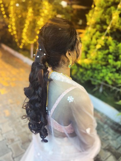 A stylish and modern ponytail with curls and pearl accents, perfect for a sangeet or cocktail party.