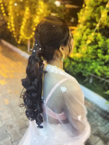 A whimsical and romantic ponytail hairstyle. The combination of braids and curls, accented with small pearls, is perfect for an outdoor evening event.