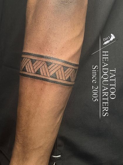 A classic tribal armband with a woven or braided pattern, inked with clean lines on the forearm.