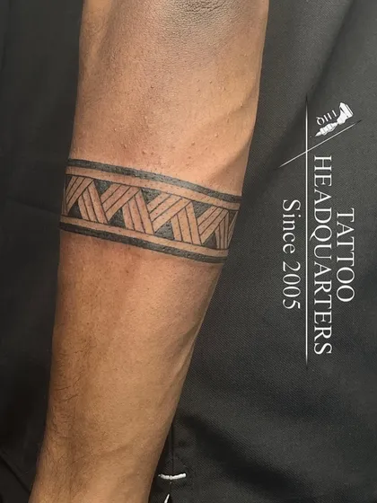 A classic tribal armband with a woven or braided pattern, inked with clean lines on the forearm.