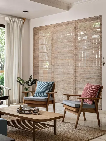 Another view of the living area, where the focus is on natural light and materials. The wooden armchairs and textured rug create a comfortable and relaxed atmosphere, perfect for conversation or quiet reading.