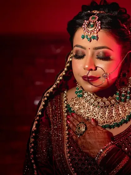 A dramatic, close up bridal portrait with a red light cast upon her, highlighting her stunning makeup and jewelry.