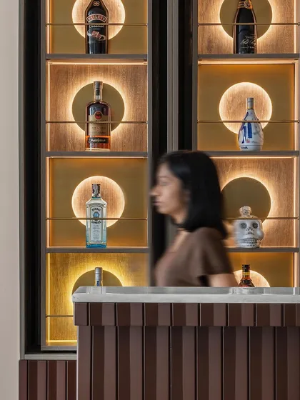 A close-up of the custom bar unit, where functionality meets artistry. Each segment features spinning shelves with backlit brass discs, transforming the bar into a captivating focal point that is both a storage solution and a statement piece.