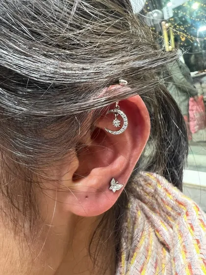 A crescent moon hanging from the helix, paired with a simple butterfly stud for a dreamy and whimsical look.