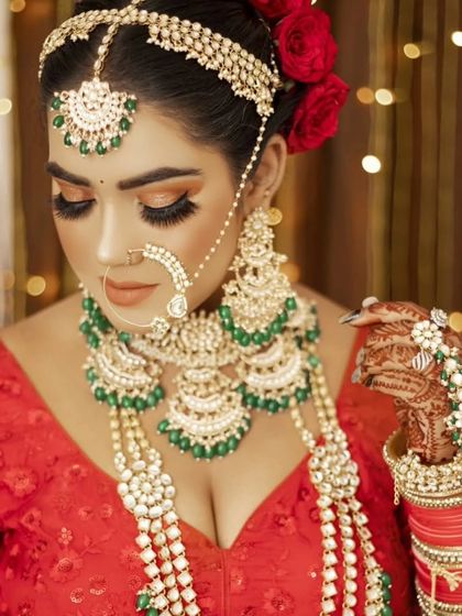 A breathtaking bridal look featuring a heavy Kundan set with green beads, paired with a red lehenga. The matching hathphool and oversized nath complete this regal ensemble.