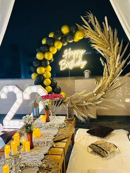 A close-up of the terrace party decor, focusing on the balloon and pampas grass arch. The combination of black and gold balloons with dried grasses creates a modern and chic aesthetic.