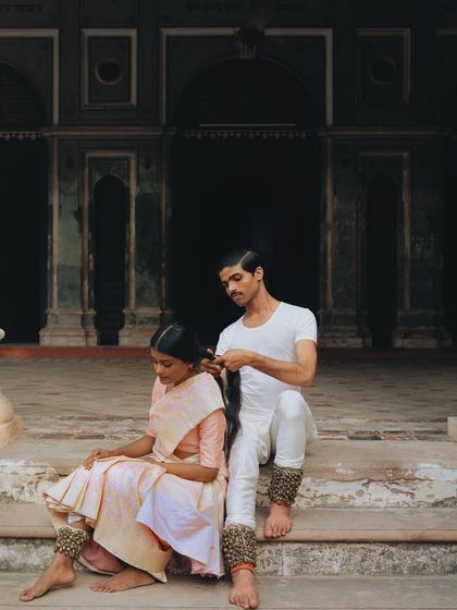 An intimate moment of preparation between two dancers. The simple white costumes and traditional ghungroos (ankle bells) are central to the story of their craft.