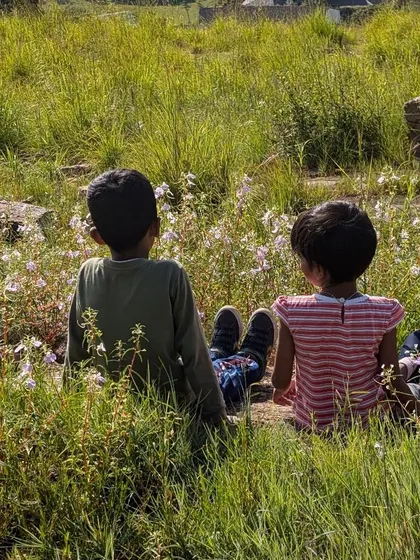 Sometimes the best moments are the quiet ones. Two young friends sit together in a field of wildflowers, a peaceful pause during one of our Tiny Trekkers adventures.