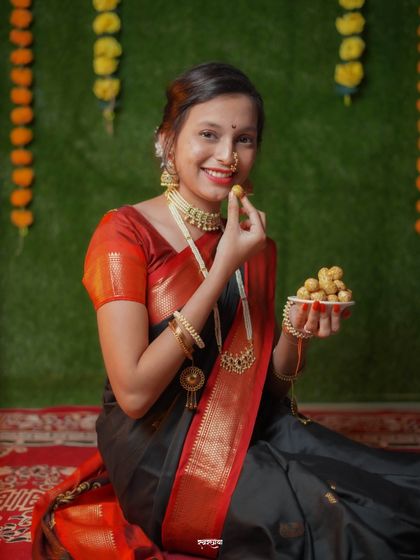 "Tilgul ghya, god god bola." This photo captures the essence of Makar Sankrant, as she happily eats a tilgul laddu. The indoor setup with a marigold backdrop adds to the festive feel.