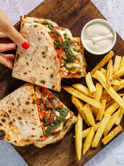 A folded pizza or calzone served with fries. The shot is styled on a rustic wooden board, giving it an authentic, artisanal feel. The pesto and cheese filling looks fresh and flavorful.