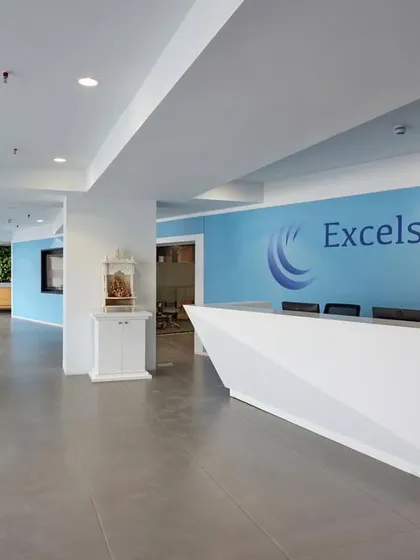 The reception for Excelsource features a faceted, geometric desk that creates a sculptural focal point. The company's brand color is used on the back wall for a clean, corporate identity.