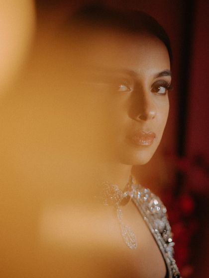 A striking close-up of the bride, with a warm, golden light flare in the foreground. Her direct gaze and the artistic framing make this a powerful and captivating portrait.