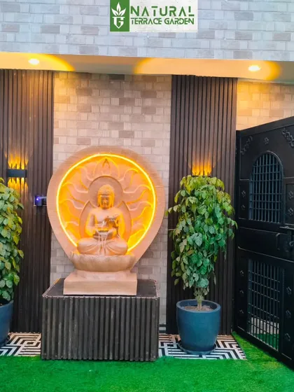 A serene entrance to a terrace garden in Uttam Nagar, New Delhi. This completed project features a custom-lit sandstone Buddha statue, flanked by lush plants, creating a tranquil and welcoming focal point for the outdoor space.