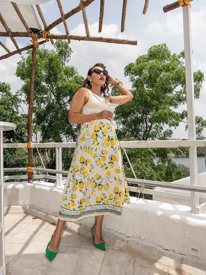 A full-length fashion shot at Olive Bistro, showcasing a lemon-print skirt against the restaurant's white architecture. The image connects fashion with a beautiful location.