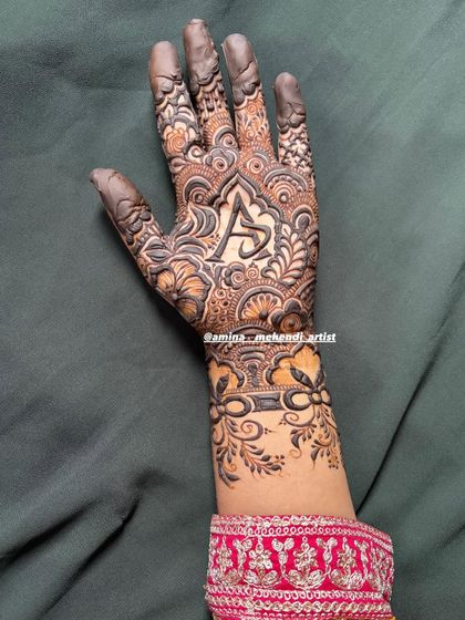 A single-hand design featuring the initial 'A' as the central element, surrounded by dense floral and paisley patterns.