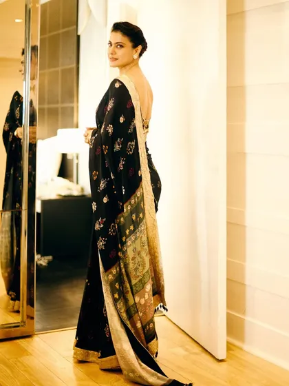 This full-length shot showcases the beautiful drape and the contrasting pallu of the black embroidered saree, reflecting a classic and graceful silhouette.