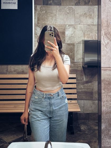 A simple and casual college look with a crop top and light-wash jeans, captured in a mirror selfie.