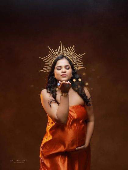 A regal portrait of a mother-to-be in a satin orange gown, complete with a golden crown. Blowing glitter adds a touch of magic to the shot.