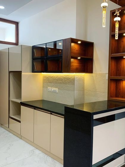 We designed this kitchen with high-gloss laminate, a breakfast counter, and wood-finish paneling to highlight the space. The open shelves with profile lighting add both storage and ambiance.
