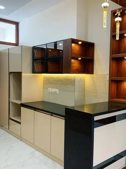 We designed this kitchen with high-gloss laminate, a breakfast counter, and wood-finish paneling to highlight the space. The open shelves with profile lighting add both storage and ambiance.