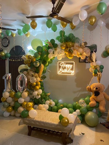 A lush green and gold jungle-themed balloon ring for a 10th birthday. This home setup includes a teddy bear prop and silver foil number balloons, creating a sophisticated take on a fun theme.