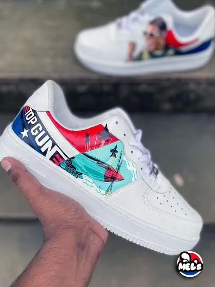 A hand-held view of the 'Top Gun' sneaker, with the Tom Cruise portrait shoe blurred in the background. This highlights the dynamic jet illustration.