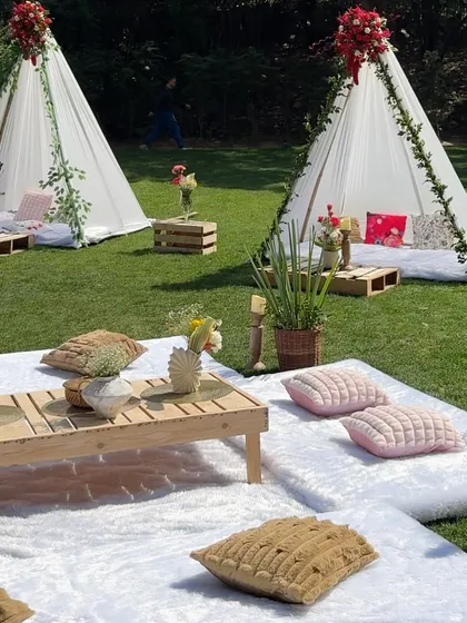 We bring the luxury picnic to you. This setup on a private lawn features cozy teepees, low wooden tables, and plush cushions, creating a relaxed yet incredibly stylish atmosphere for a sun-kissed afternoon gathering.
