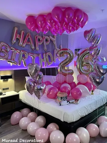 A stylish and romantic birthday surprise in a modern room. The decoration uses shades of pink and silver, with heart-shaped balloons and large number balloons for the age.