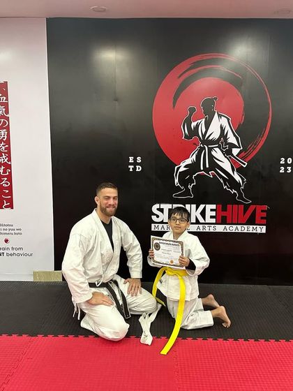 A young student poses with his coach and new certificate after a successful belt test. We foster a close bond between our coaches and students.