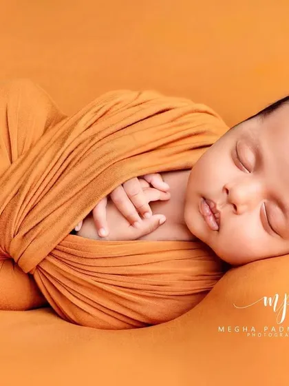 A side-view of the baby wrapped in a mustard-yellow swaddle, showing their peaceful profile.