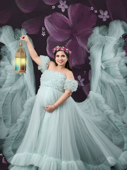 A magical and whimsical portrait. The mother-to-be holds a lantern, her face lit with a gentle smile, surrounded by the fantasy-like wings of her blue gown.