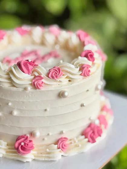 A close-up of the mini vintage anniversary cake, showing the texture of the buttercream and the tiny edible pearls scattered among the pink rosettes.