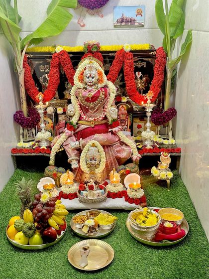 A beautiful Varamahalakshmi decoration where the Goddess is draped in a shimmering pink silk saree, surrounded by fruits and flowers.