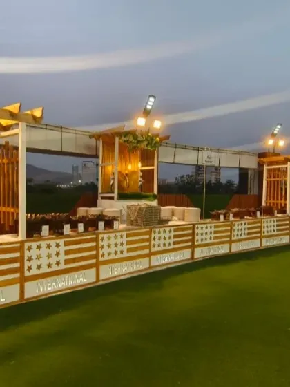 An outdoor lawn setup offers a unique charm for evening events. This is the dining area on the lawn at Ellora Banquet hall in Sanpada, featuring a modern wooden pergola design and elegant buffet counters.