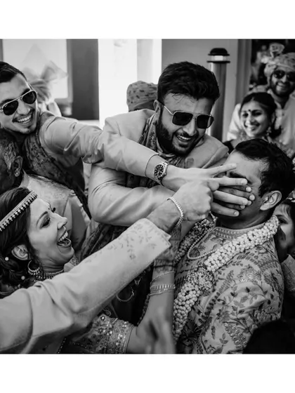 Tirth's friends playfully make it hard for his future mother-in-law to reach his nose during a ritual. This black and white shot captures the fun and mischief of wedding games.