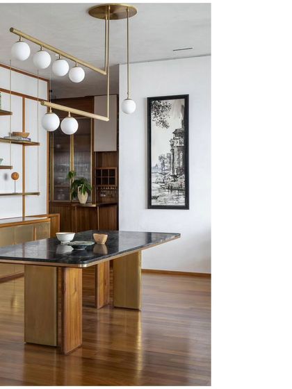 The dining area of the 'Ikigai House', featuring a custom-designed table with a stone top and solid wood base. The suspended brass shelving unit behind it is another bespoke piece, designed to feel light and airy.