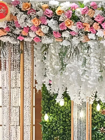 A close-up of a lush floral canopy, showing the rich texture of pastel roses, cascading white wisteria, and sparkling crystal strings.
