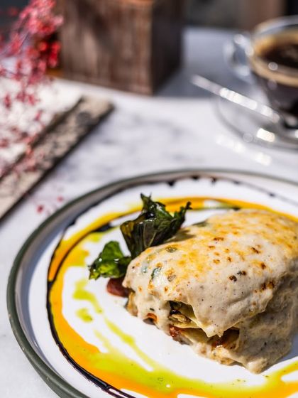 A beautifully plated slice of lasagna, with sauces artfully swirled around it. This dish is perfect with a cup of coffee for a leisurely lunch.