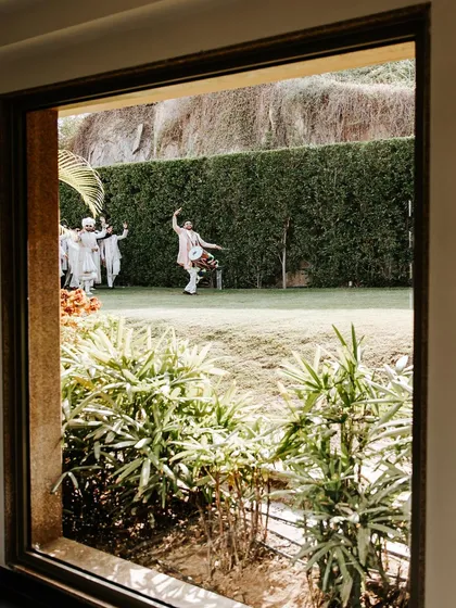 A glimpse of the groom's baraat procession, viewed from a window. This shot captures the anticipation and excitement that builds throughout the day at a destination wedding.